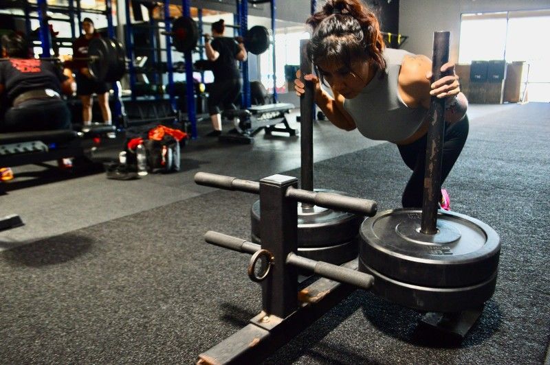 A woman is pushing a sled with weights in a gym.