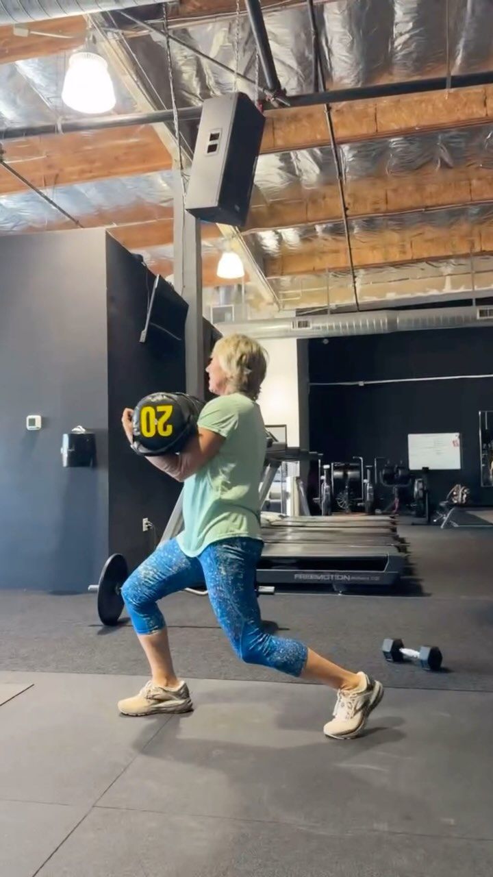 A woman is doing lunges with a medicine ball in a gym.