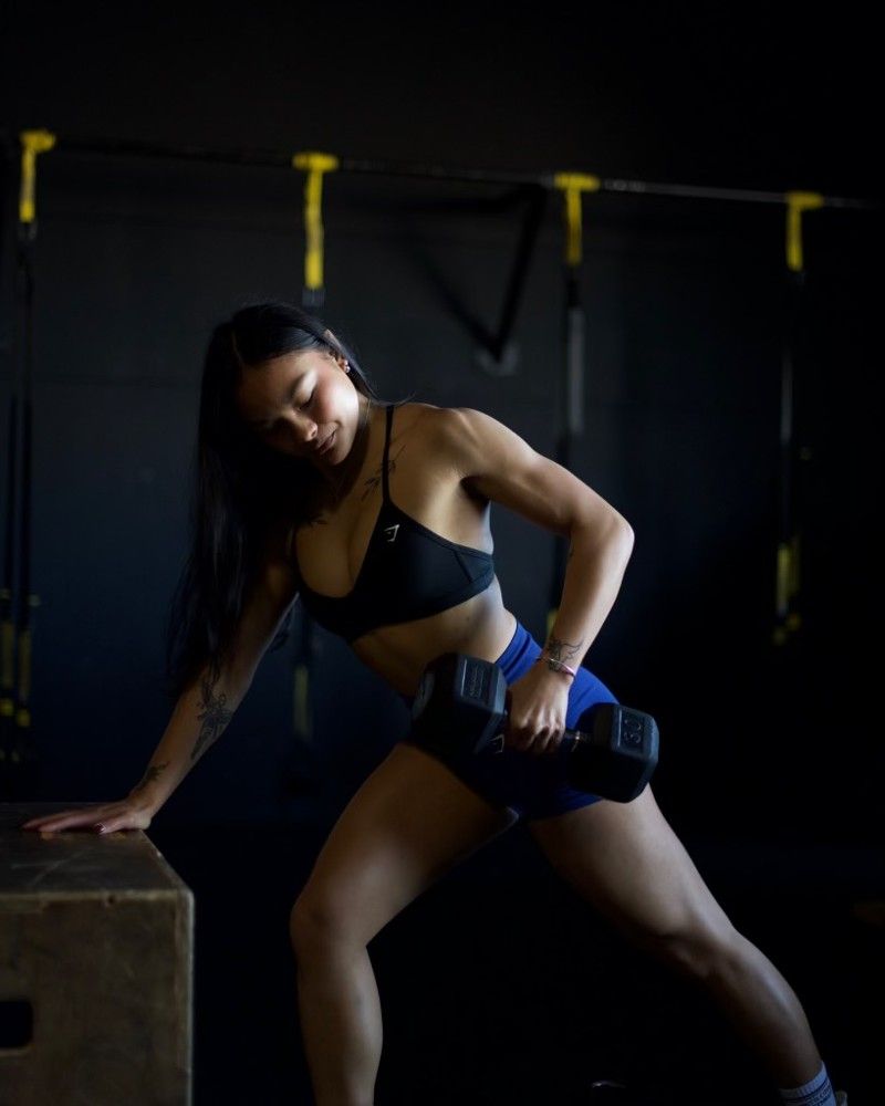 A woman in a black bra and blue shorts is holding a dumbbell