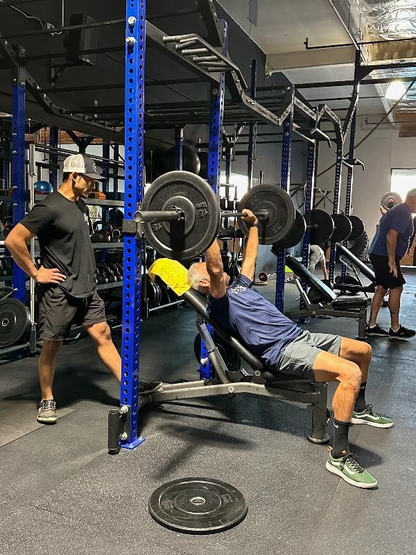 A man is lifting a barbell on a bench in a gym.