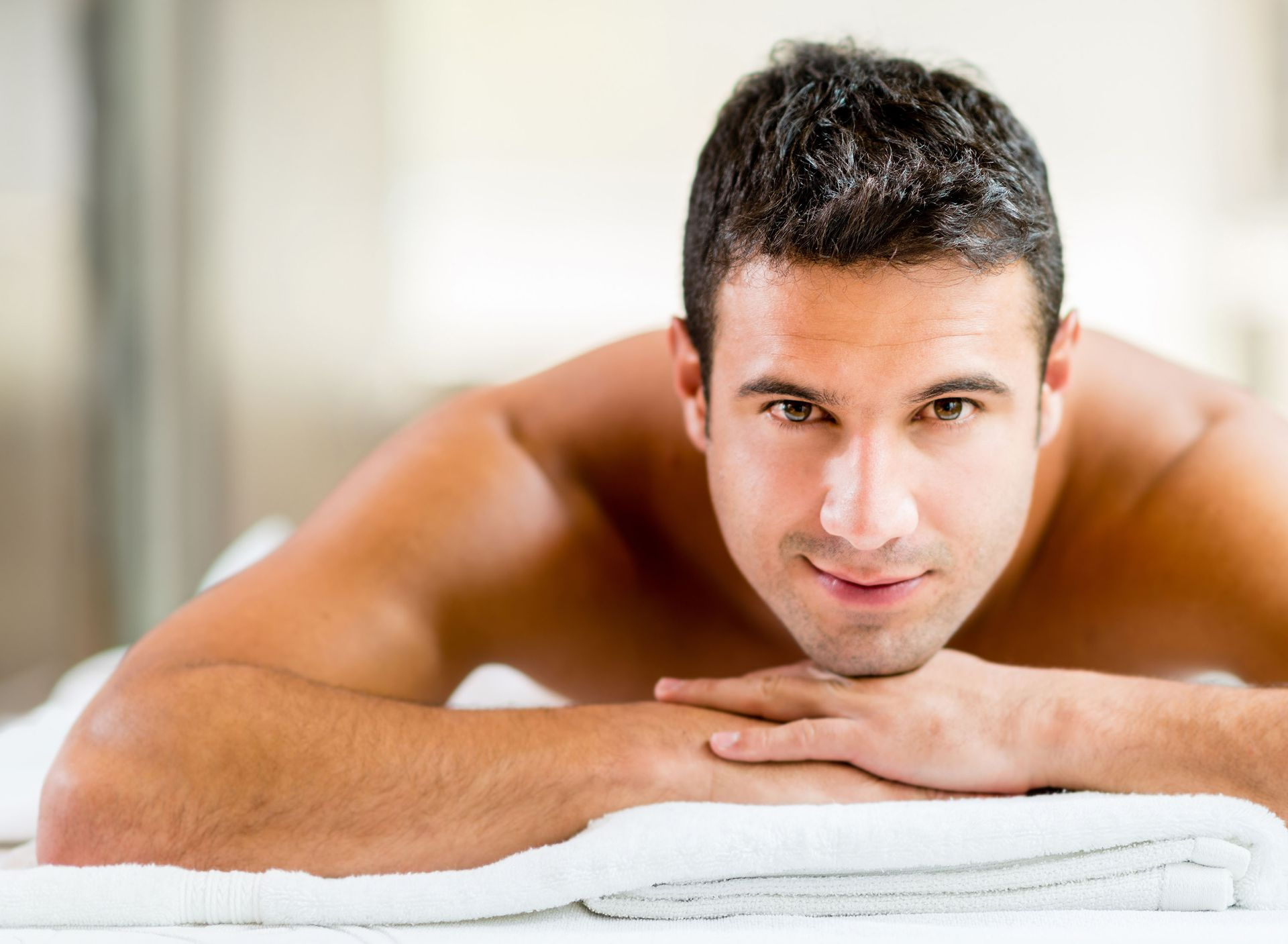 A smiling person lying prone on a white towel during a massage session.