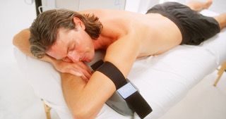 A person lying on a massage table with a therapeutic heating pad strapped to their arm.