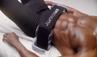 A person lying on their back with an Emsculpt device strapped over their abdominal muscles.