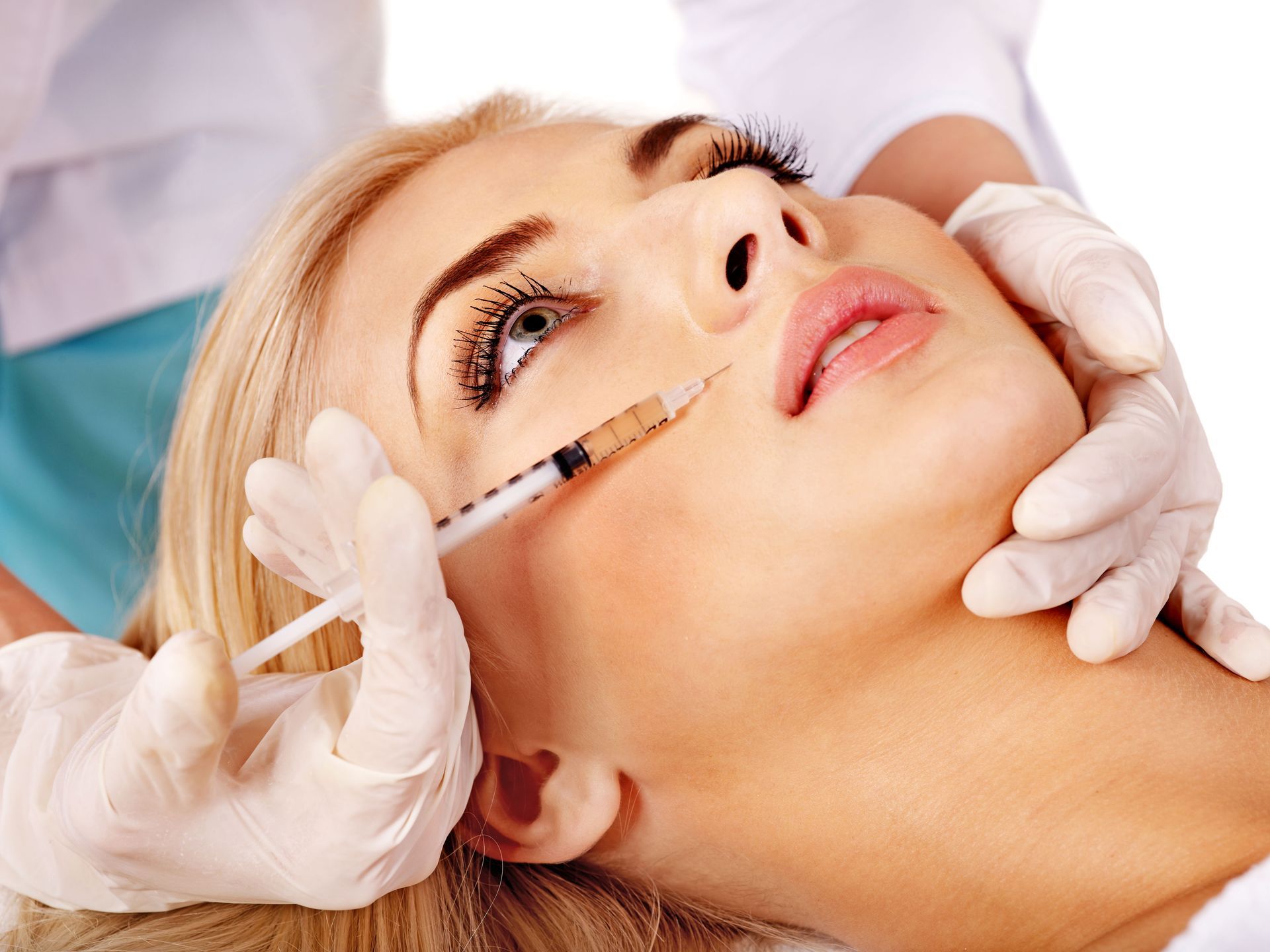 A person in bright pink medical gloves administers a cosmetic lip filler injection to a client lying on a white surface.