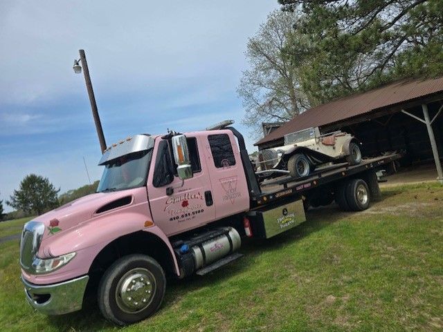 A pink tow truck is towing a golf cart in a field.