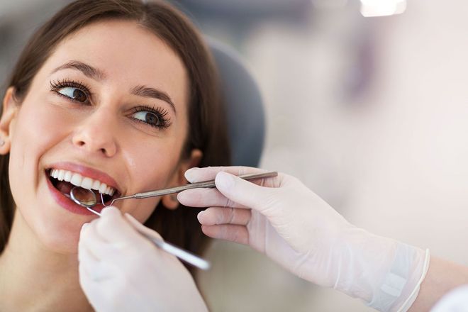 Dentist examining a smiling patient’s teeth with a mirror and gloved hands