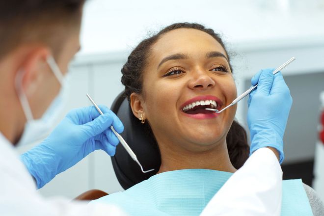 Dentist examining a smiling patient’s teeth with dental tools in a clinic