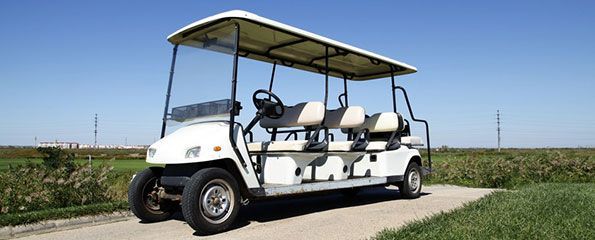 A white golf cart is parked on the side of a dirt road.