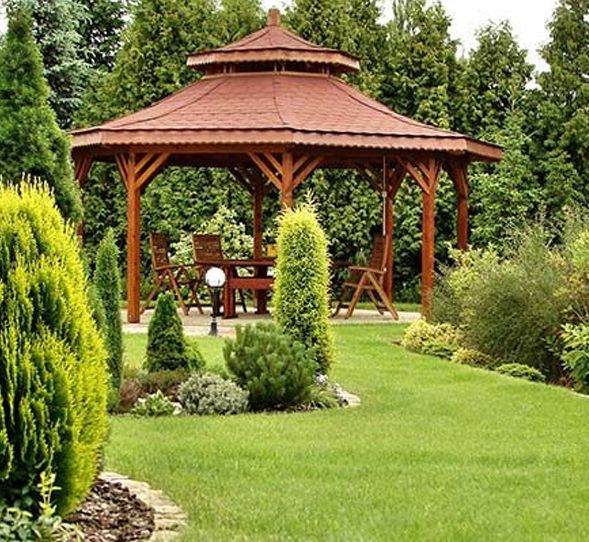 Wooden gazebo in a manicured garden, with a table and chairs inside