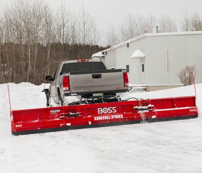 Red BOSS snowplow attached to a gray pickup truck, clearing snow from a driveway