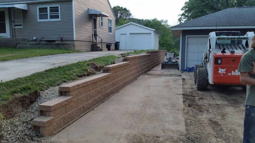 Brown retaining wall along a driveway with a skid steer loader in the background