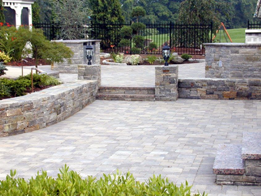 Stone patio with retaining walls, lanterns, and a black fence in a garden setting