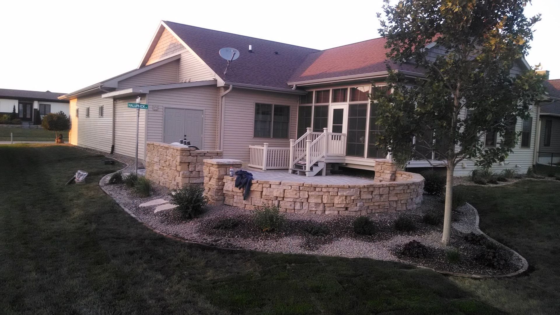Stone patio with landscaping in front of a house, partly screened porch visible