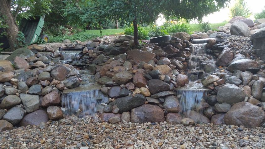 Waterfall cascading down rocks in a garden setting, with green foliage in the background