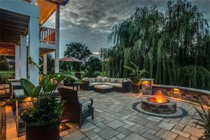 Patio with fire pit, outdoor seating, and lush greenery at dusk