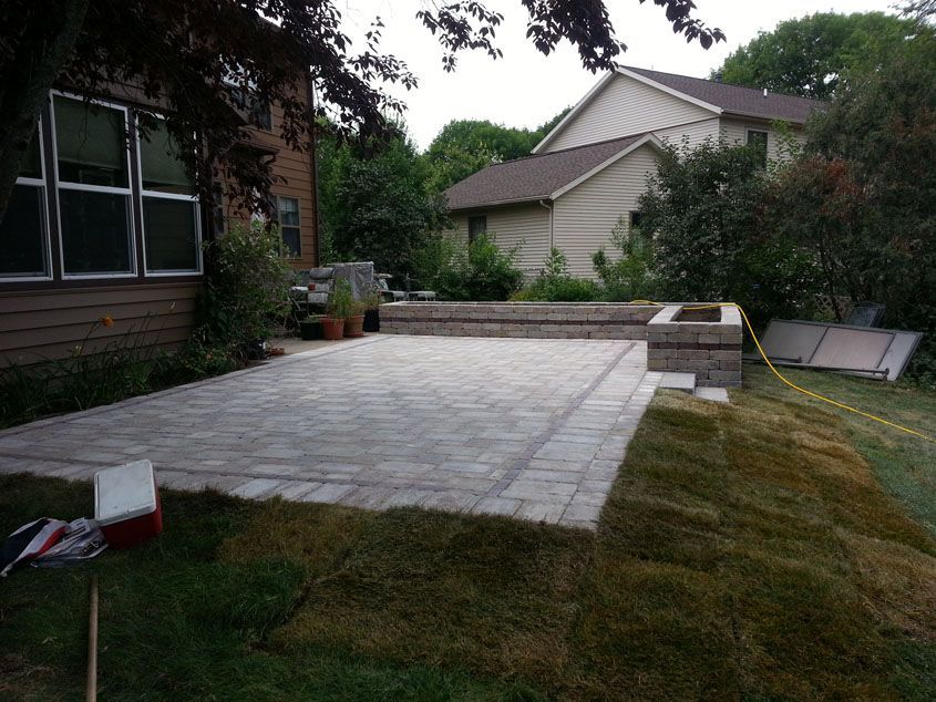 Large stone patio with retaining wall, grass, and house in the background