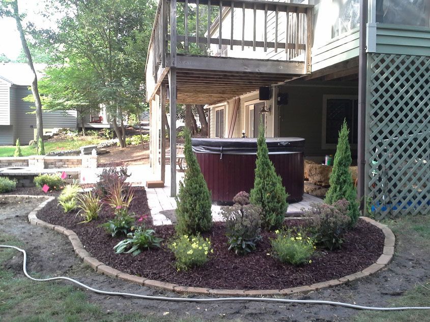 Backyard patio with hot tub, landscaping with brick edging and colorful plants, under a wooden deck