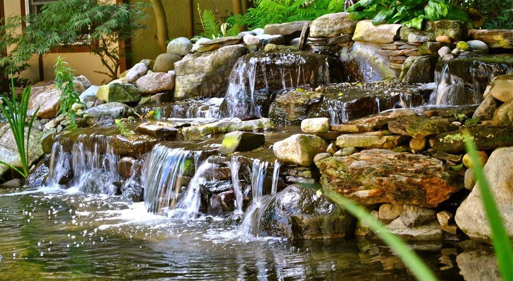 Waterfall cascading over rocks into a pond, surrounded by greenery