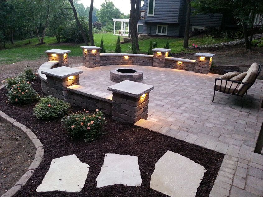 Stone patio with fire pit, seating wall, and lighting in a backyard setting