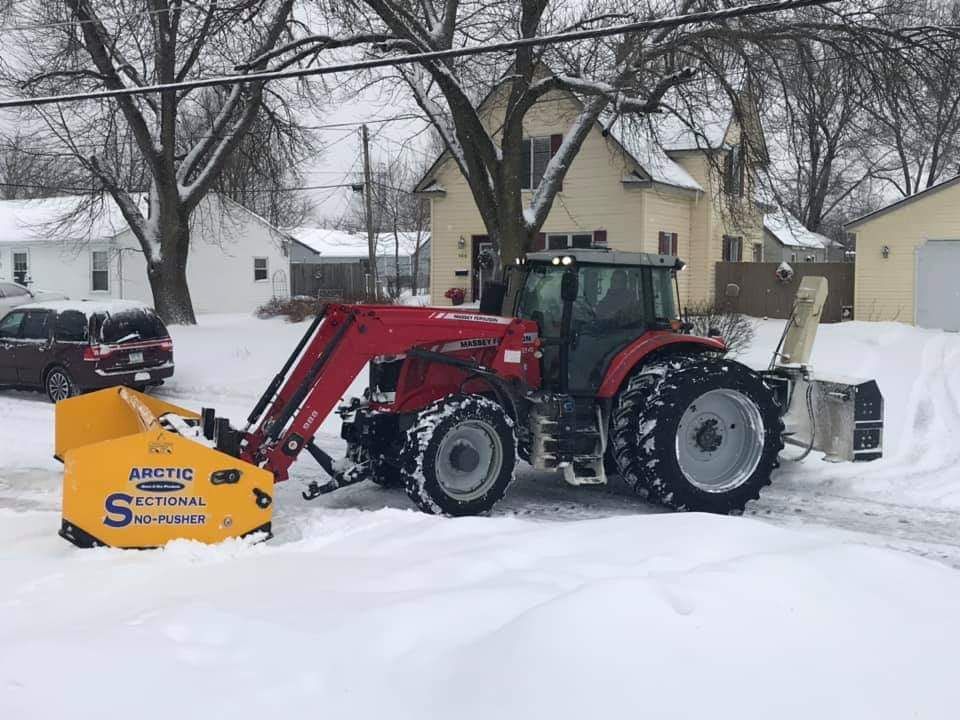 Red tractor with snowblower clearing snow in a residential neighborhood