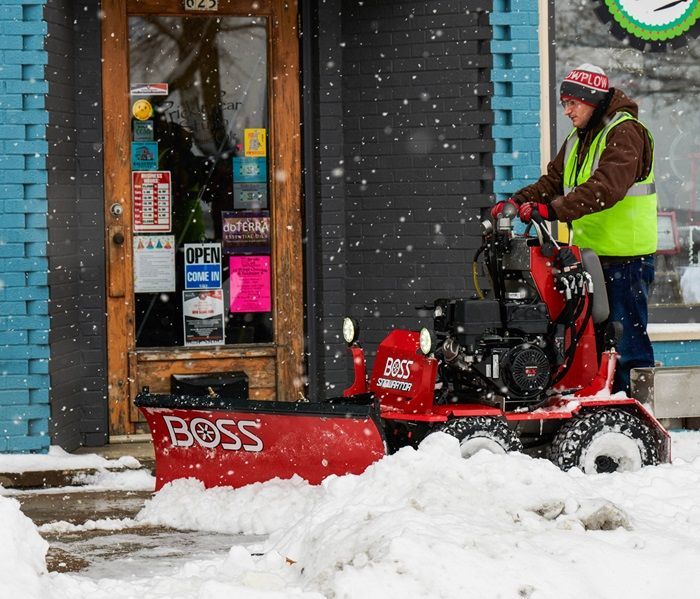 Person using red BOSS snowplow to clear snow from a storefront