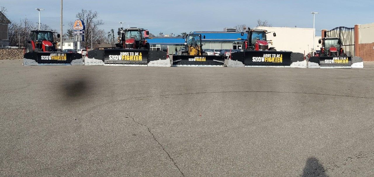 Construction equipment lined up in a parking lot. Red tractors and yellow loader sit on large gray pads.