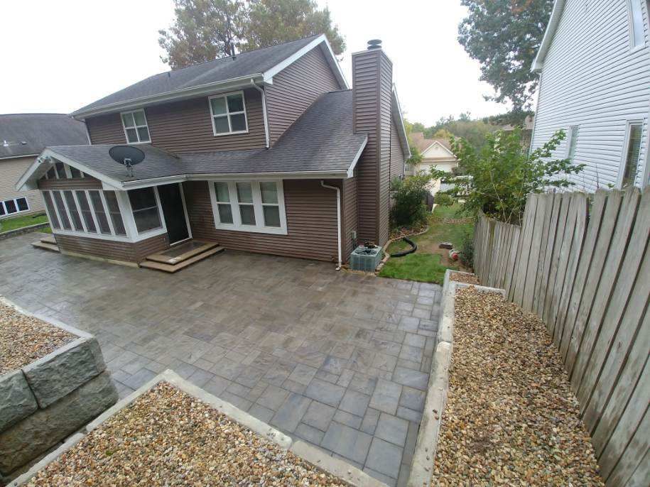 Brown house with paved patio, landscaping, and wooden fence.