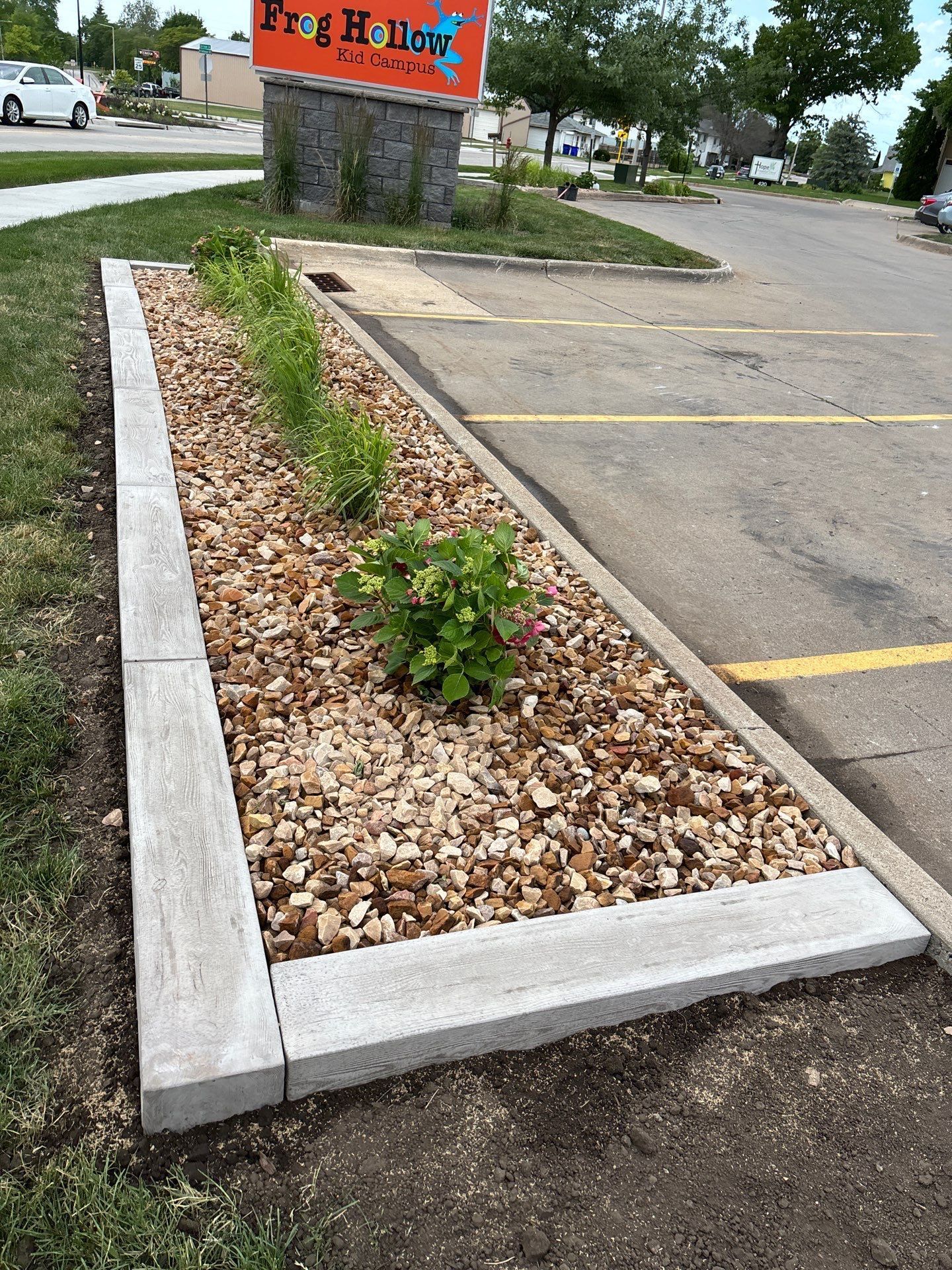 Garden bed with gravel and plants, framed with stone and bordered by concrete
