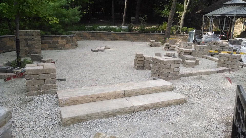 Stone patio construction with stacked blocks, gravel ground, steps, and a distant gazebo.