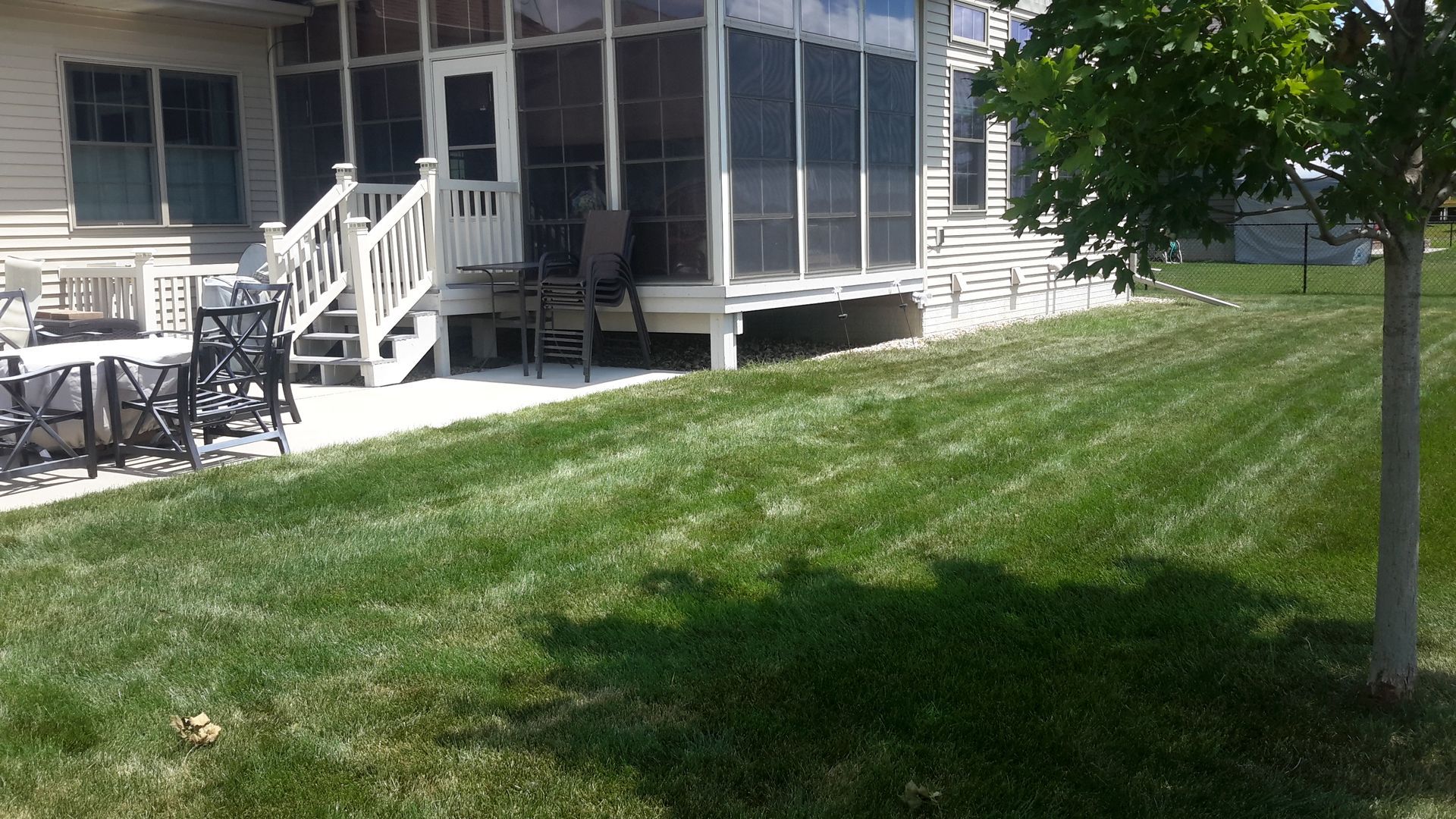 Lawn and patio area next to a house with a screened porch. Green grass and sunny day.