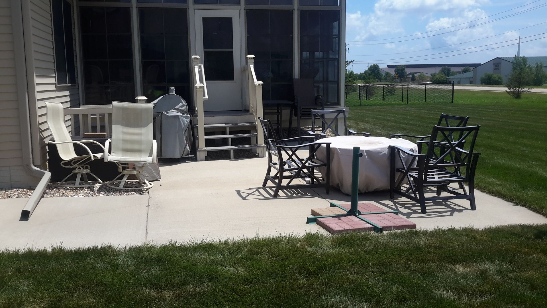 Backyard patio with chairs and table, leading to a screened-in porch, in front of a house.