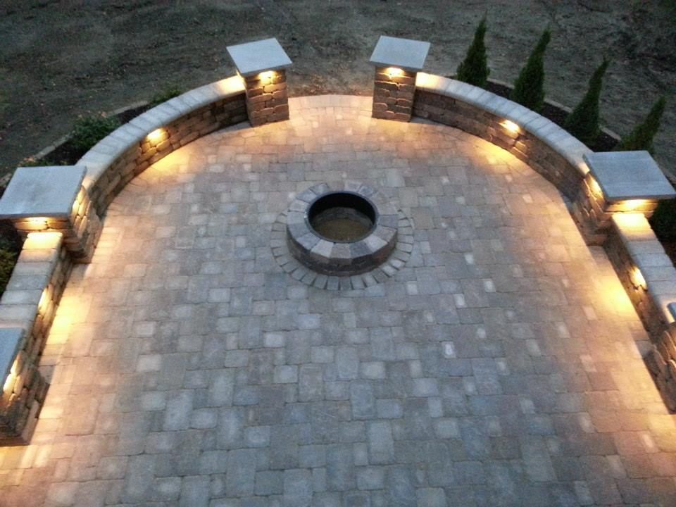 Brick patio with built-in fire pit and curved wall with illuminated pillars.