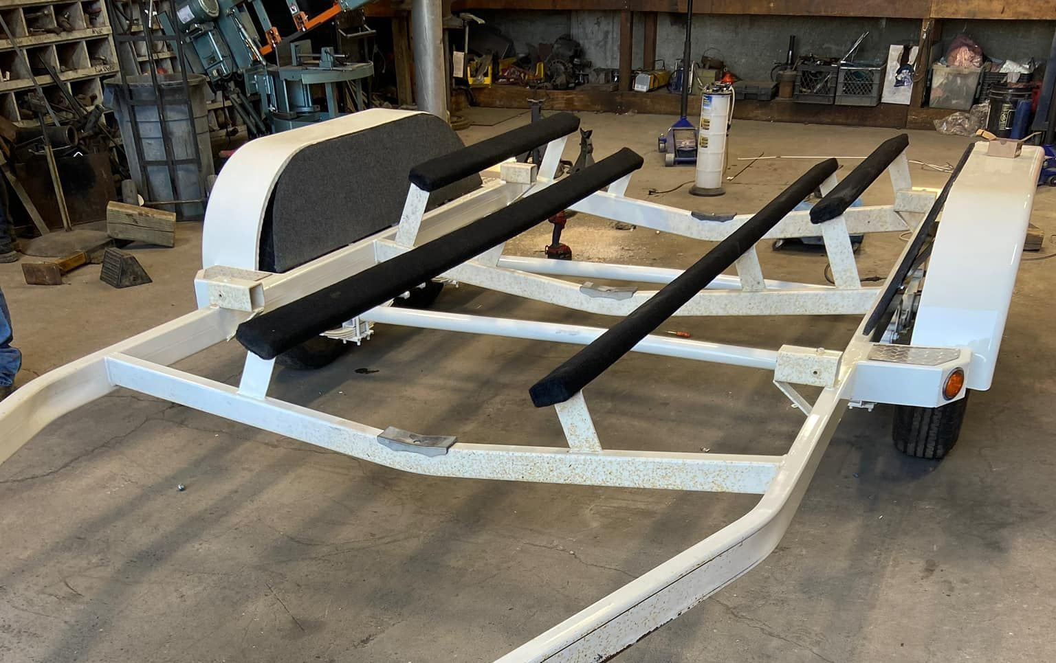 A white boat trailer is sitting on the ground in a garage.