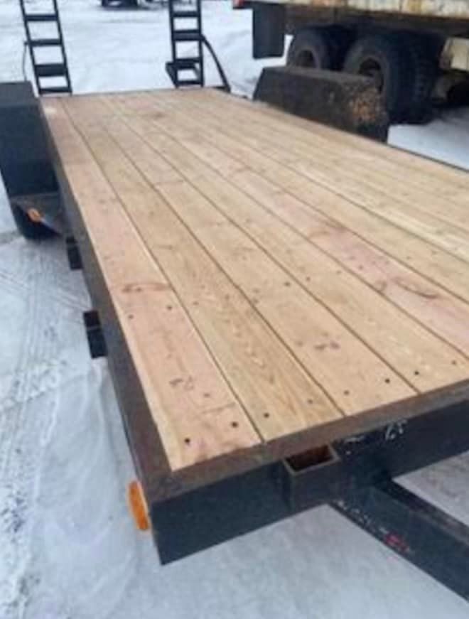 A trailer with a wooden deck is parked in the snow.