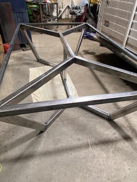 A metal table frame is sitting on the floor in a garage.