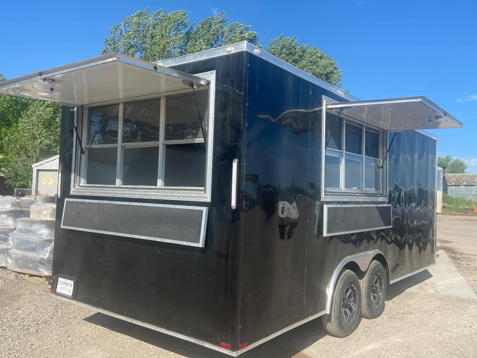 A black food truck is parked in a dirt lot with its doors open.