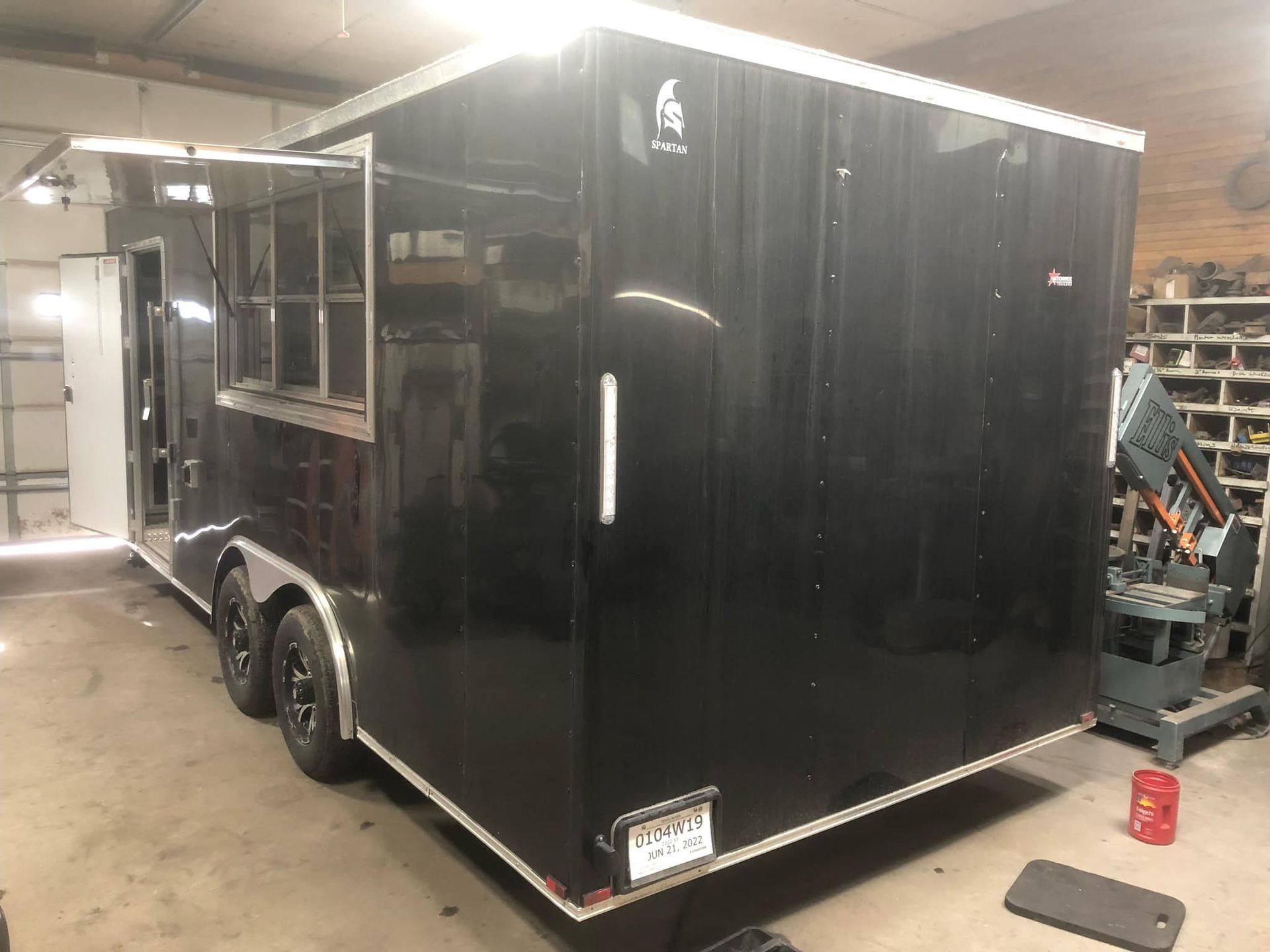 A black trailer is parked in a garage next to a machine.