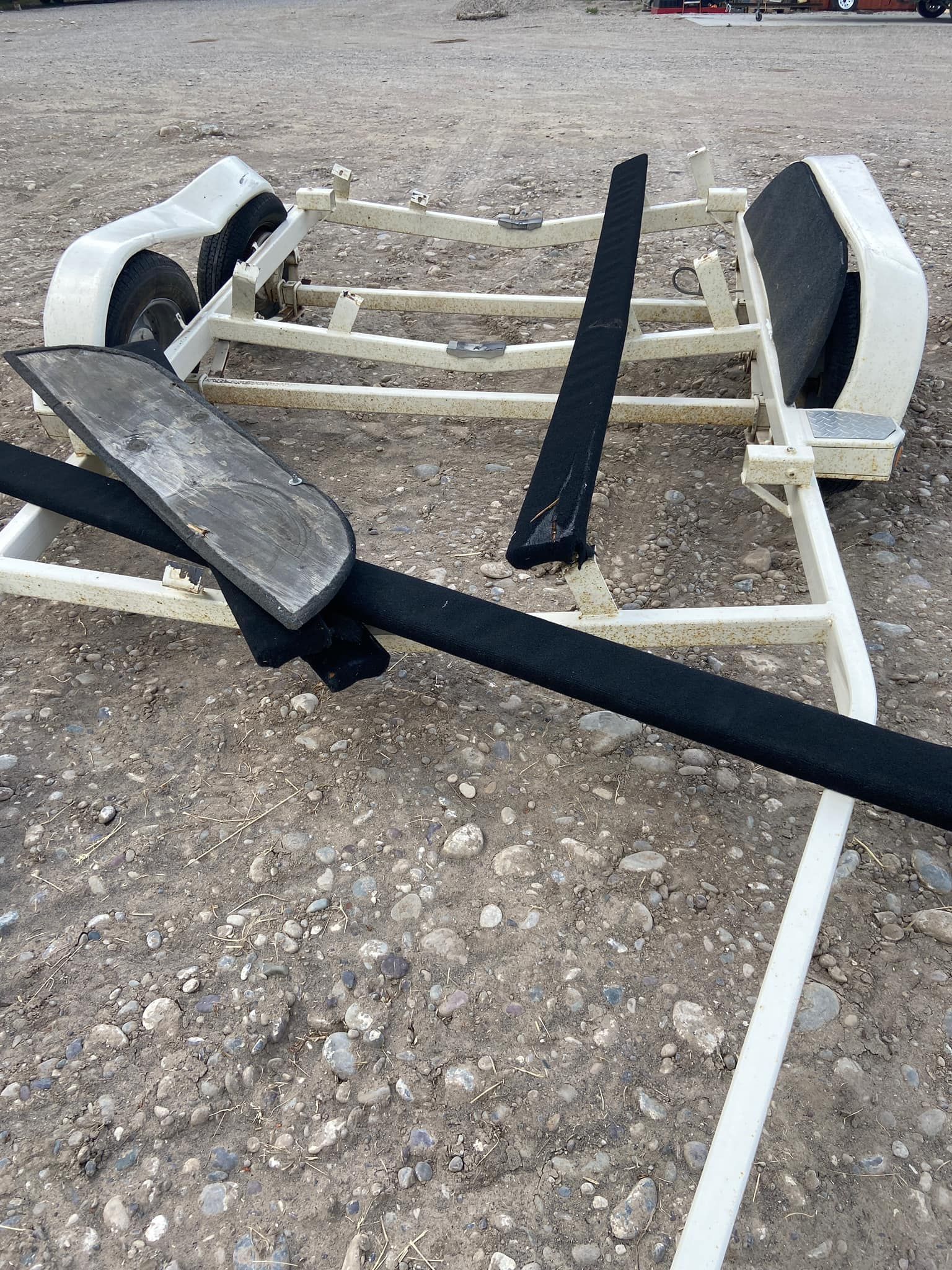 A boat trailer is laying on the ground in the dirt.