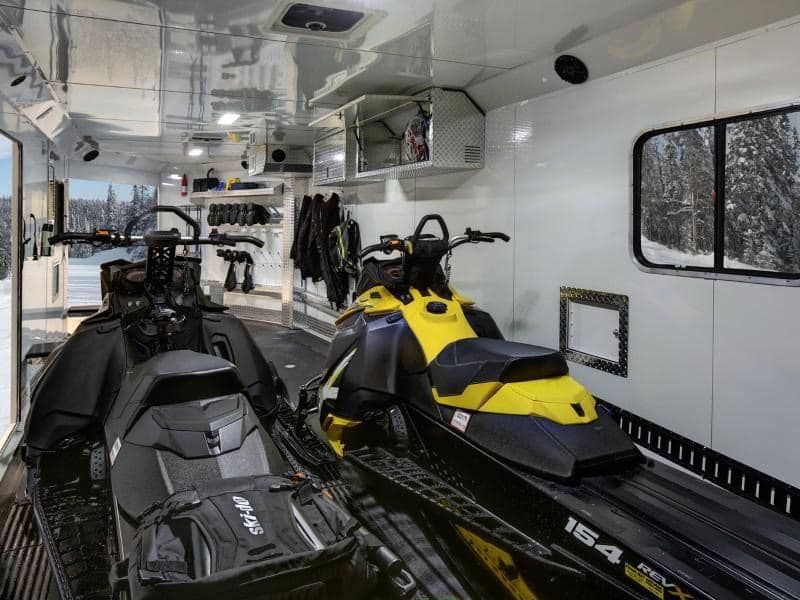 Two snowmobiles are parked in the back of a trailer