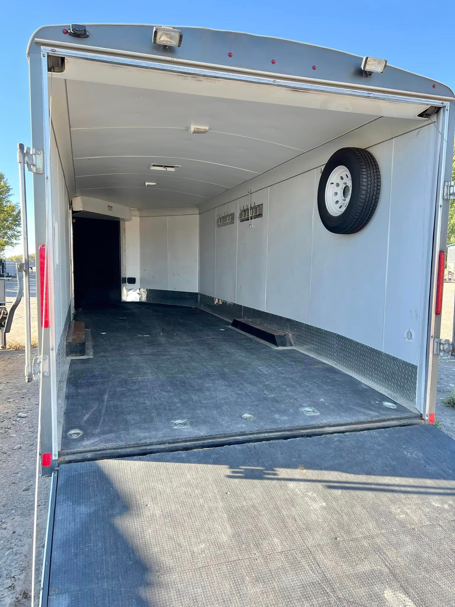 A white trailer with the door open and a tire on the side.
