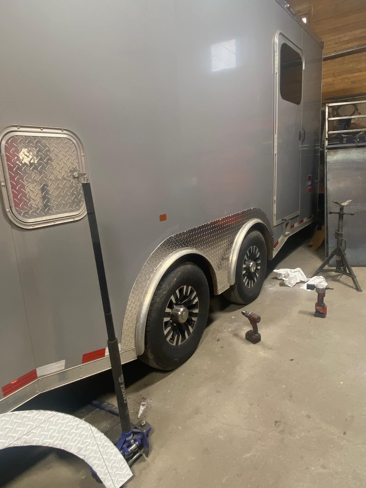 A gray trailer is parked in a garage next to a fan.