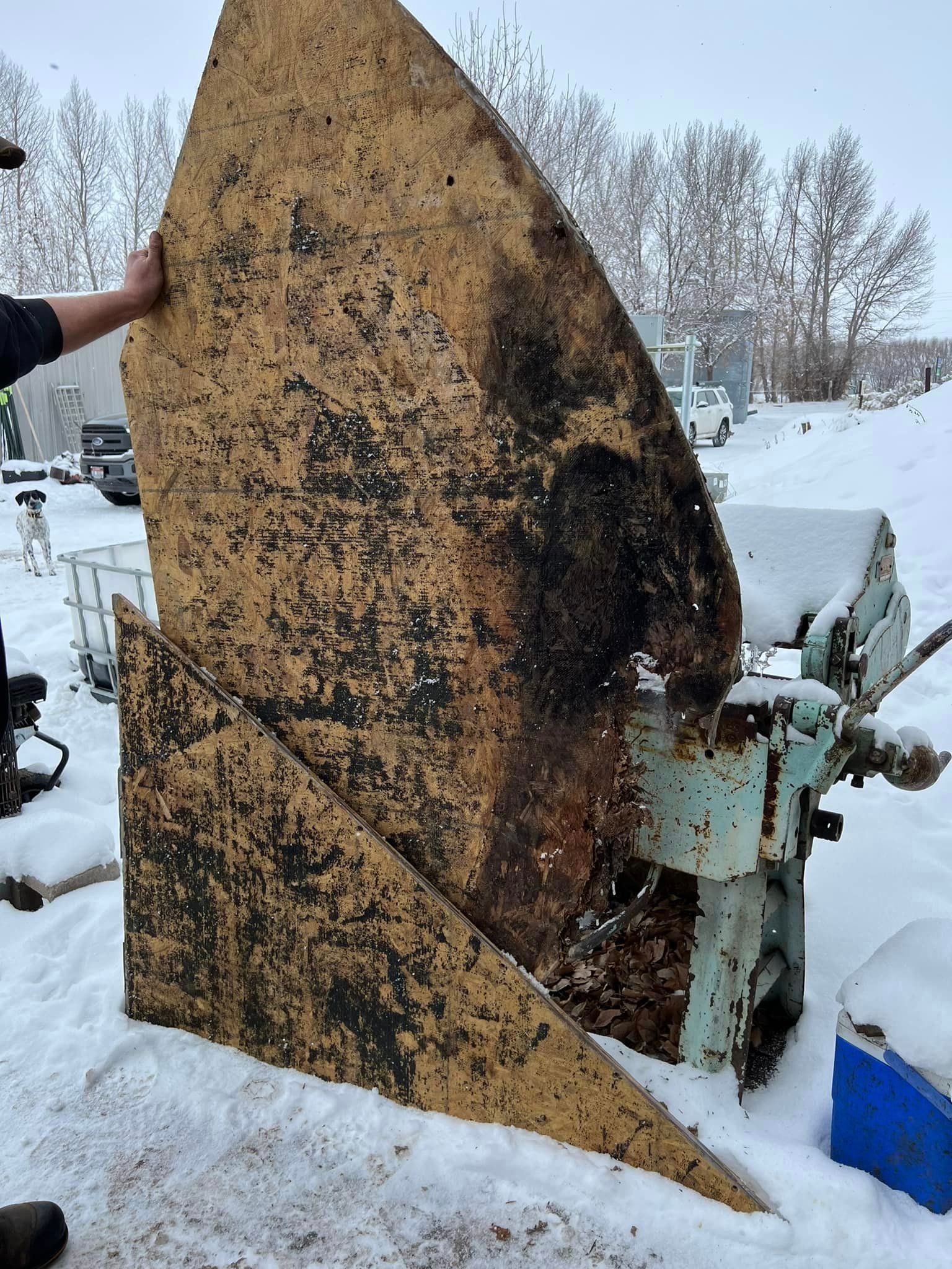 A person is holding a piece of wood in front of a machine in the snow.