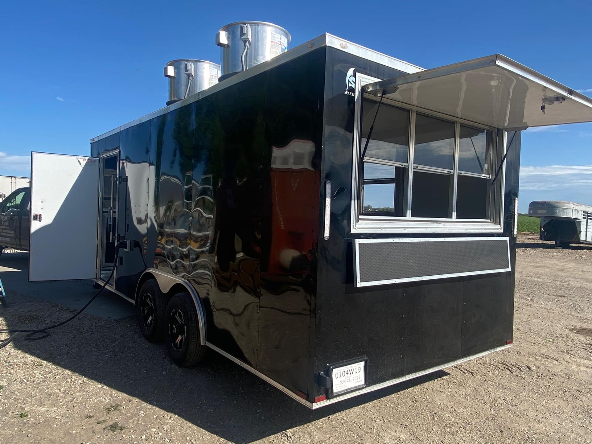 A black food truck with the door open is parked in a gravel lot.