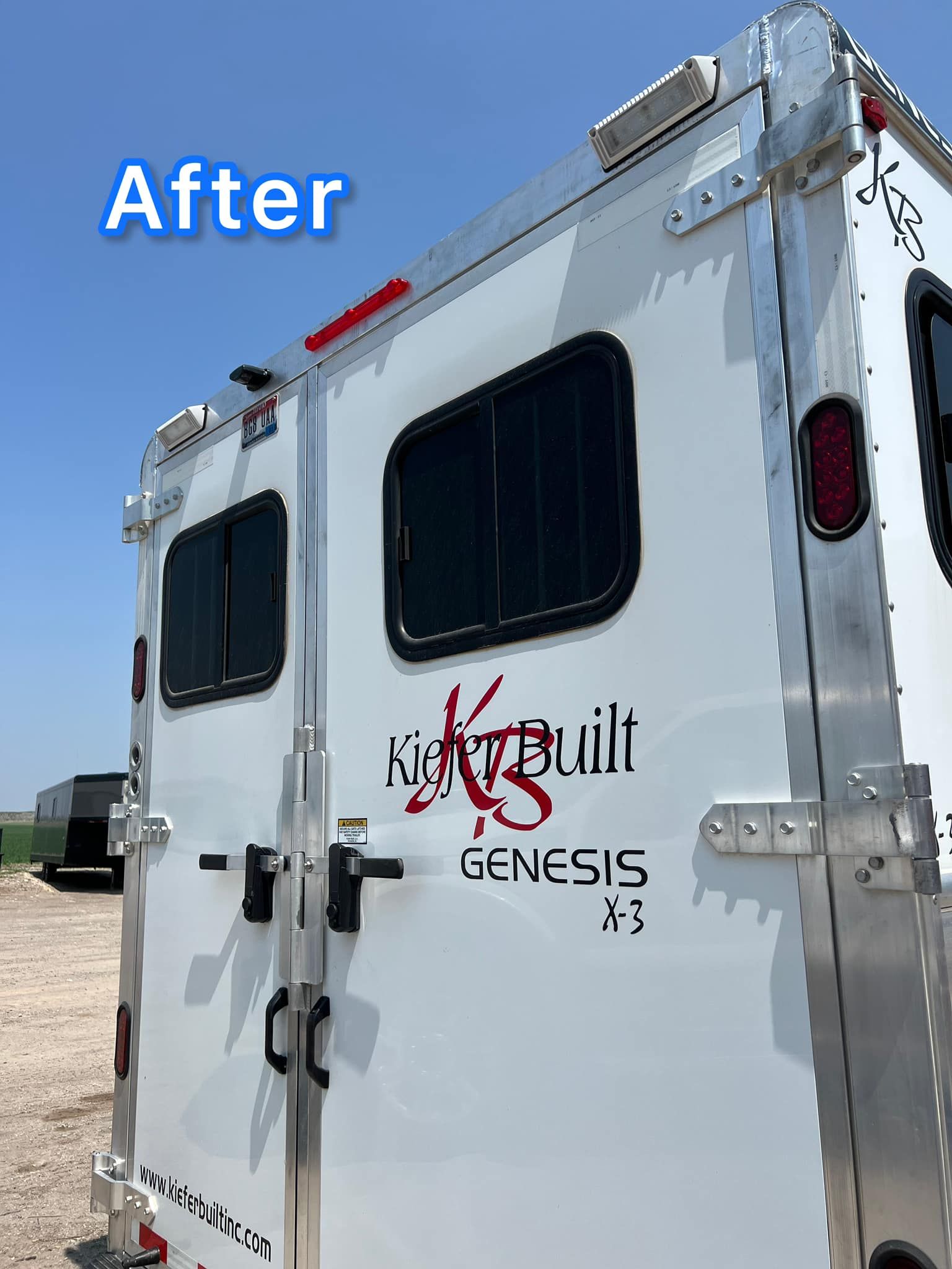 A white trailer is parked in a field with a blue sky in the background.