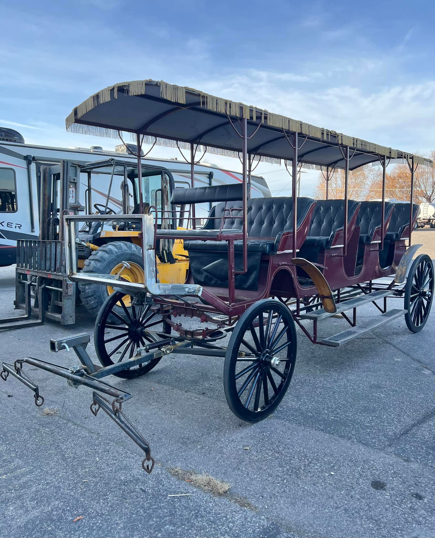 A horse drawn carriage is parked in a parking lot next to a forklift.