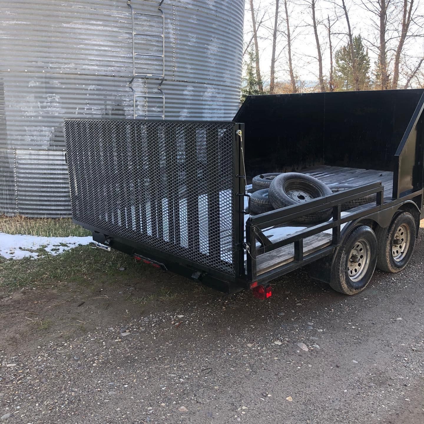 A trailer is parked on the side of the road next to a silo.
