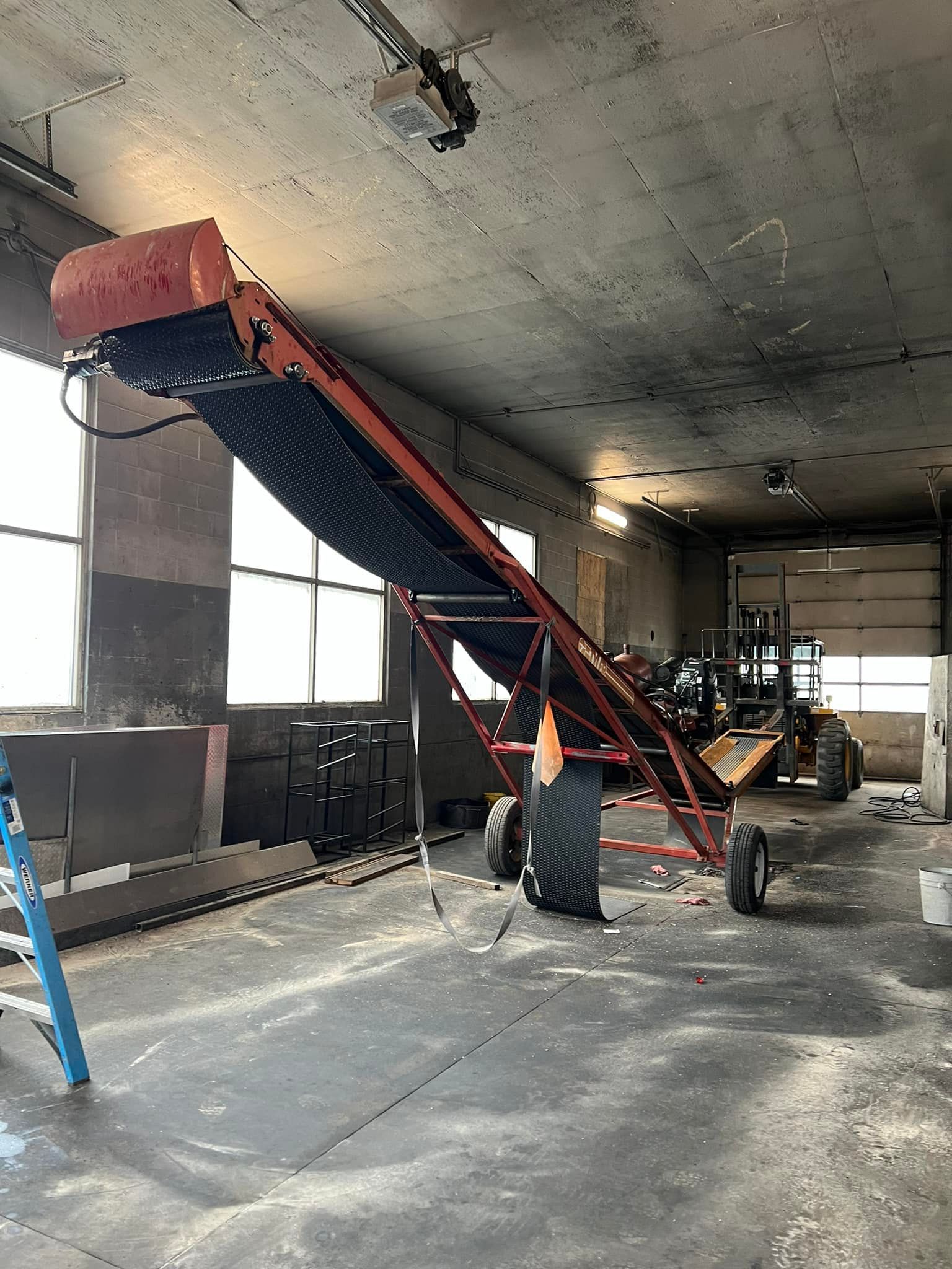 A conveyor belt is sitting in a warehouse next to a ladder.