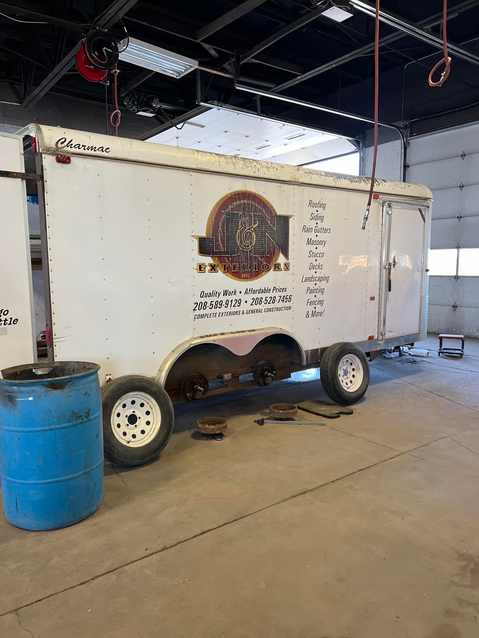 A white truck is parked in a garage next to a blue barrel.
