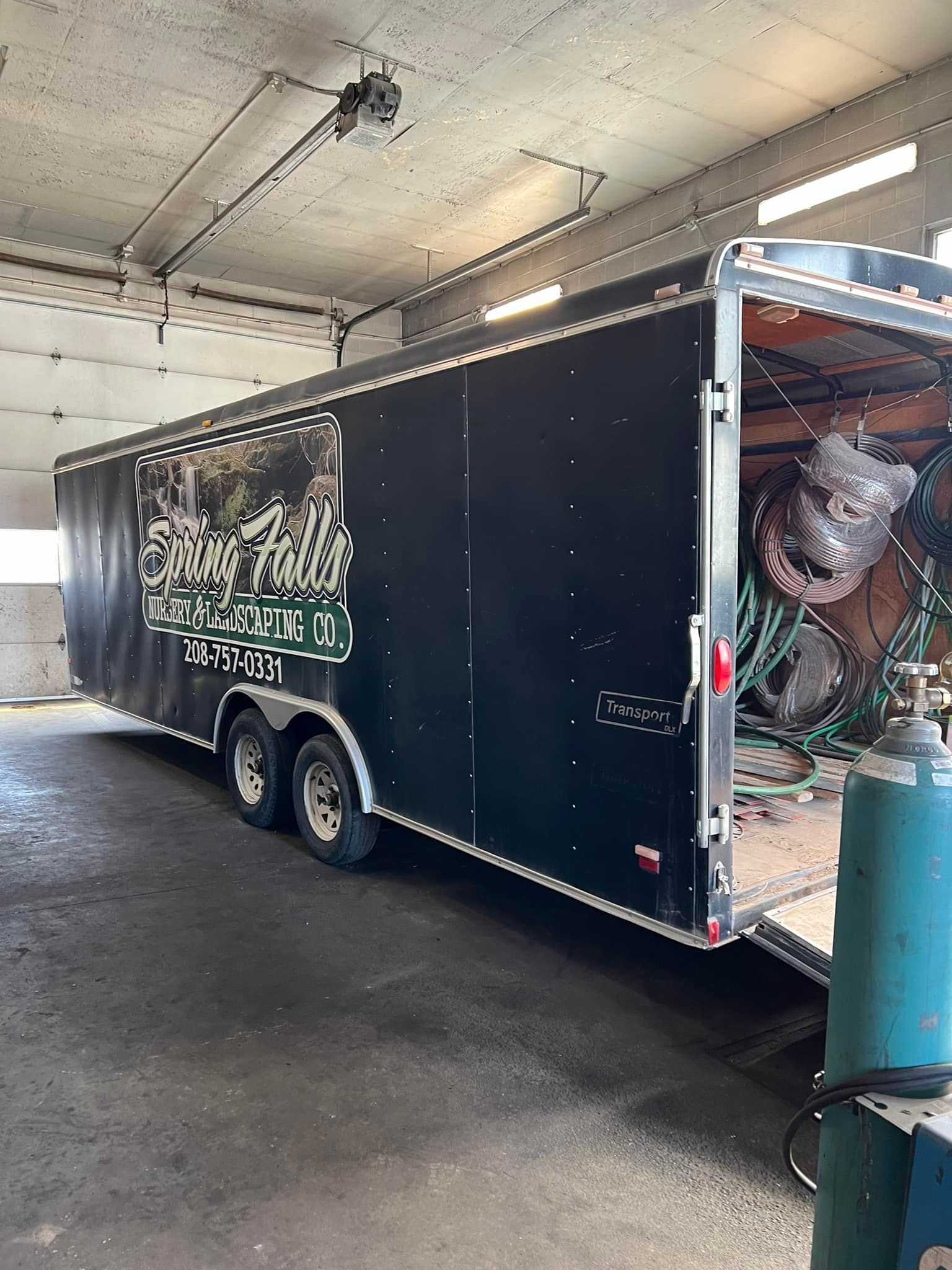 A black trailer is parked in a garage with the door open.