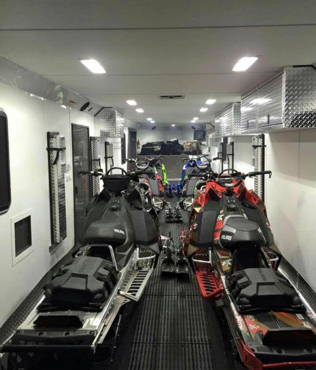 A bunch of snowmobiles are parked in a garage.